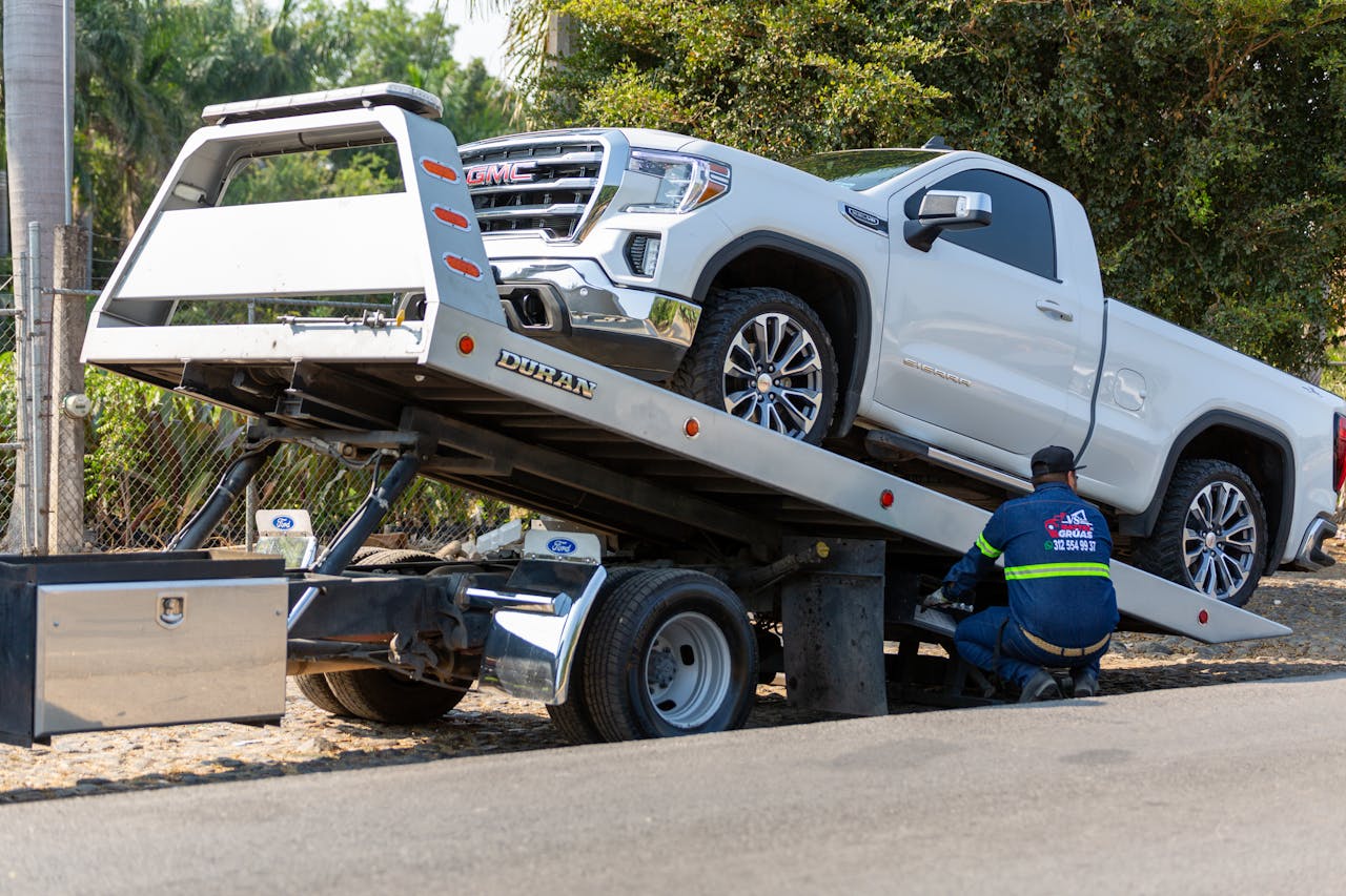 about-us Tow truck operator loading white GMC pickup truck on street in daytime.